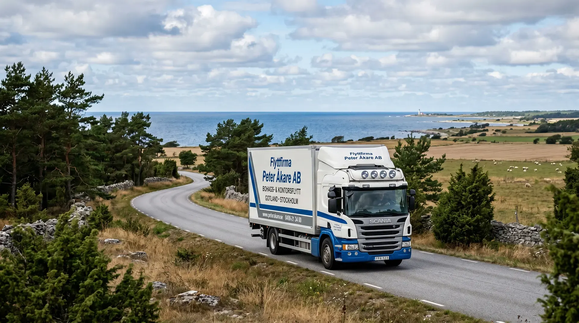 Vit lastbil från Peter Åkare AB kör längs kustväg med hav och betesmark i bakgrunden.